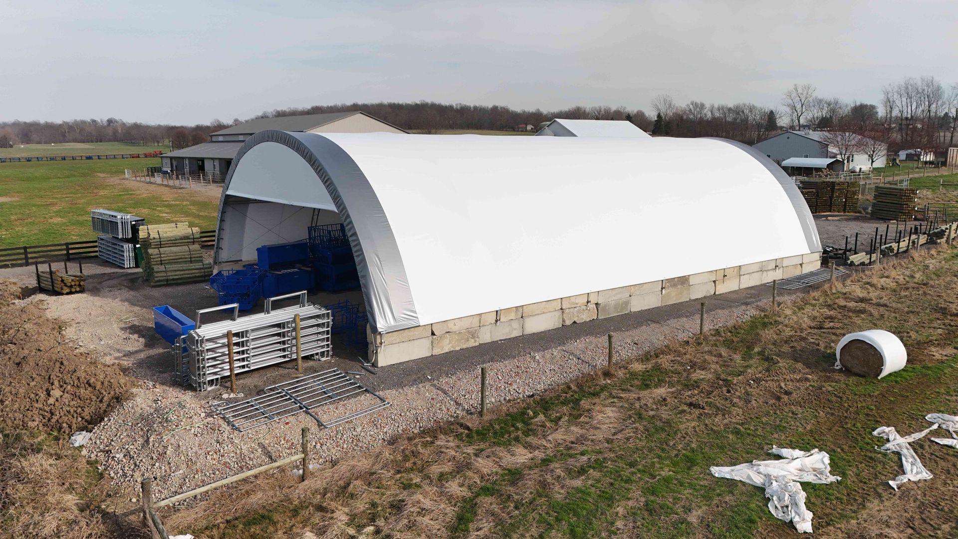 Large white arched-roof building on concrete base. Blue machinery visible inside. Outdoor setting with grass and other buildings.