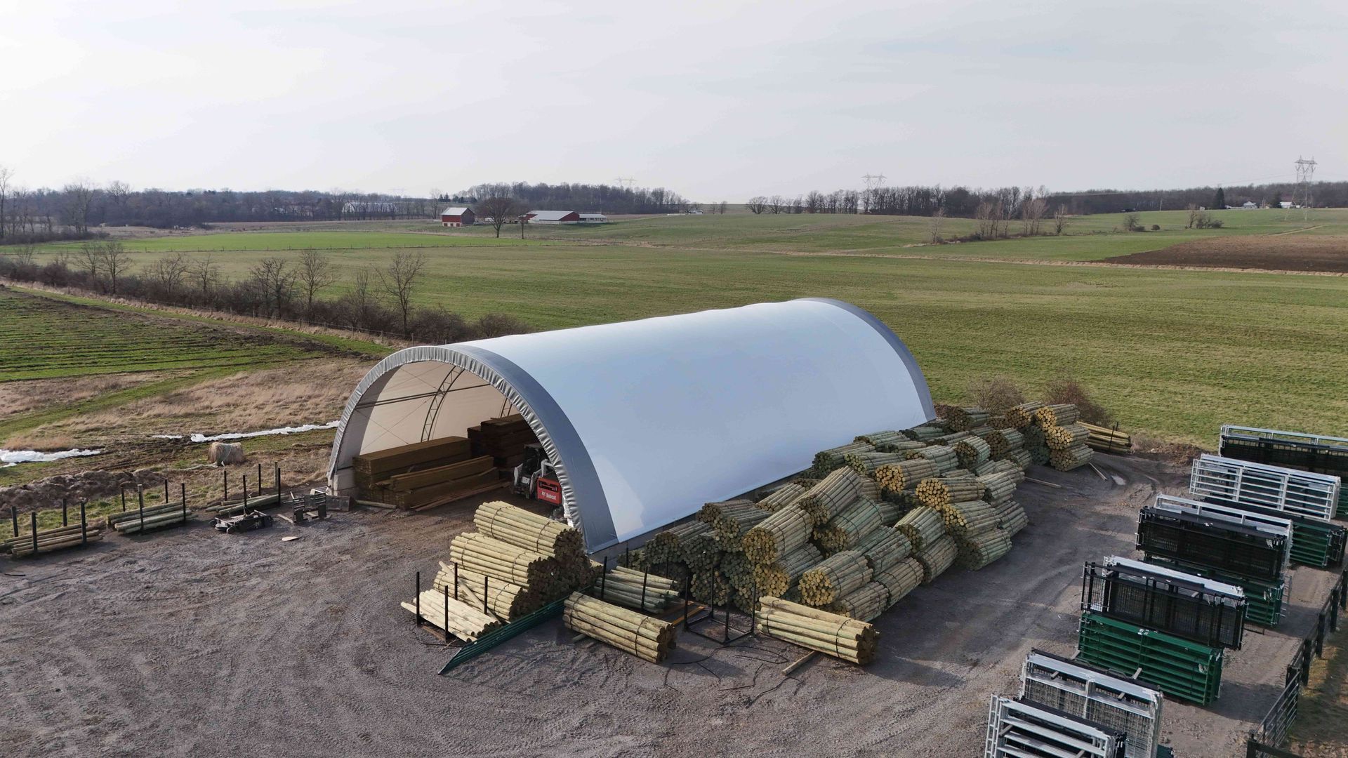 A farm scene with a white arched shelter, hay bales, and green fields.