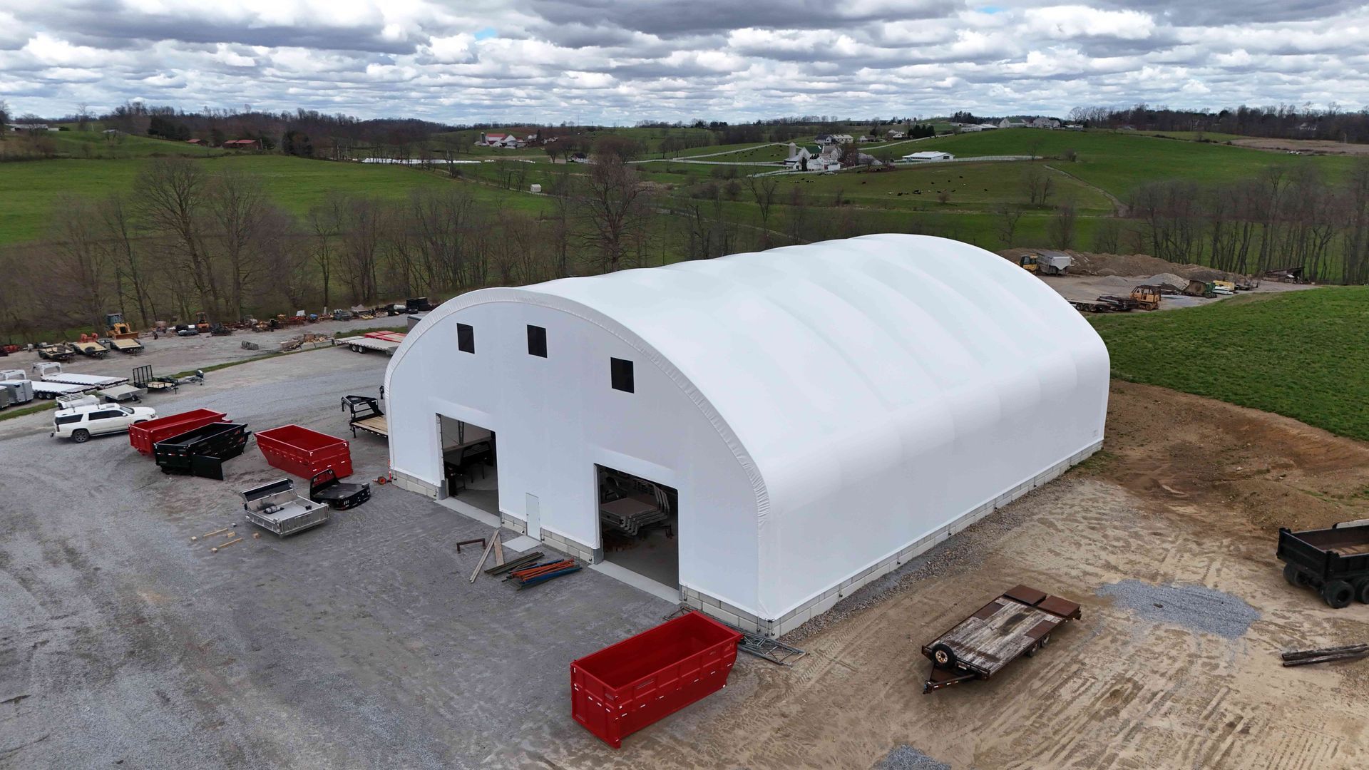 White arched-roof storage building with two open entrances, in a gravel lot with rural background.