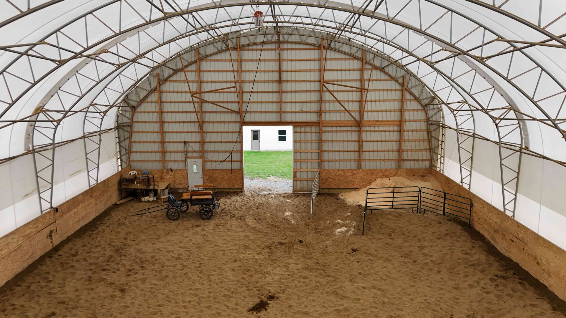 Large, open-air barn with arched roof. Interior has dirt floor and wooden walls, an open doorway in the distance.