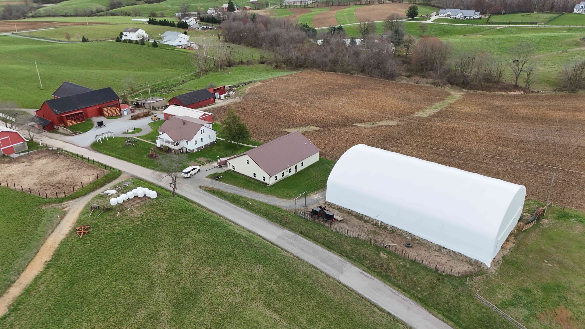 Aerial view of a farm with several buildings, fields, and a large white arched structure.