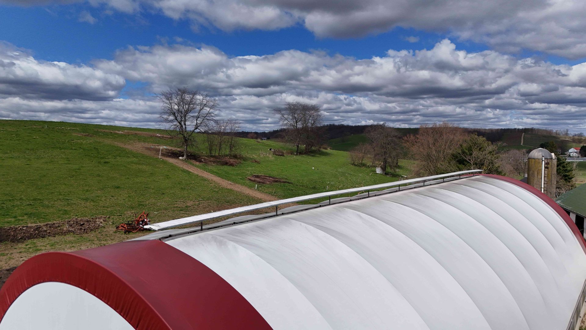 Rolling green hills under a cloudy sky, with a red-trimmed, white-arched building in the foreground.