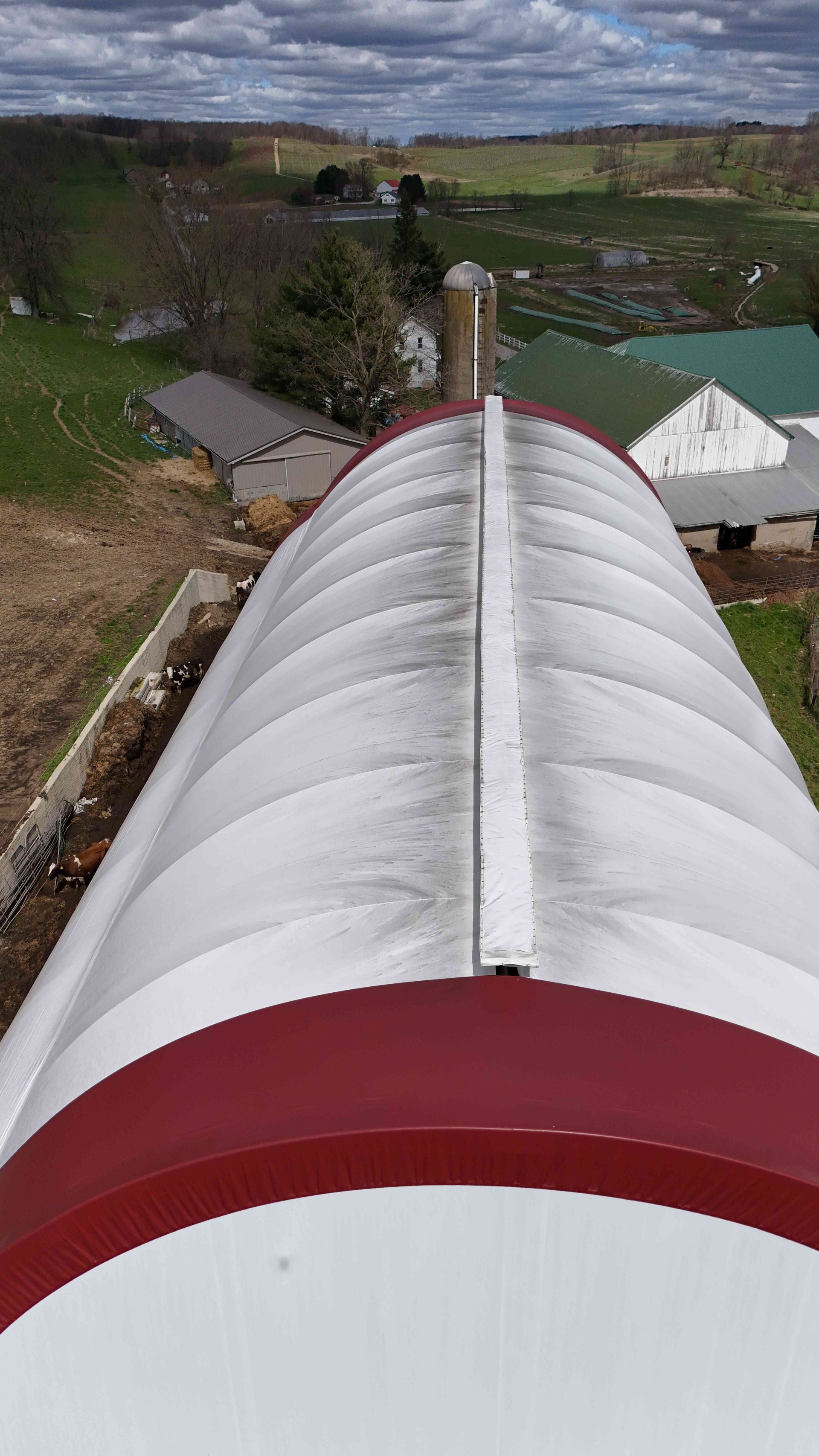 Overhead view of a curved, red and white barn roof with surrounding rural landscape.