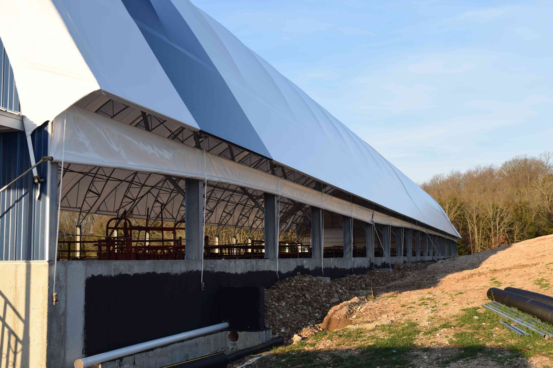 Long, covered agricultural building; white and blue roof, open sides, built on a berm.