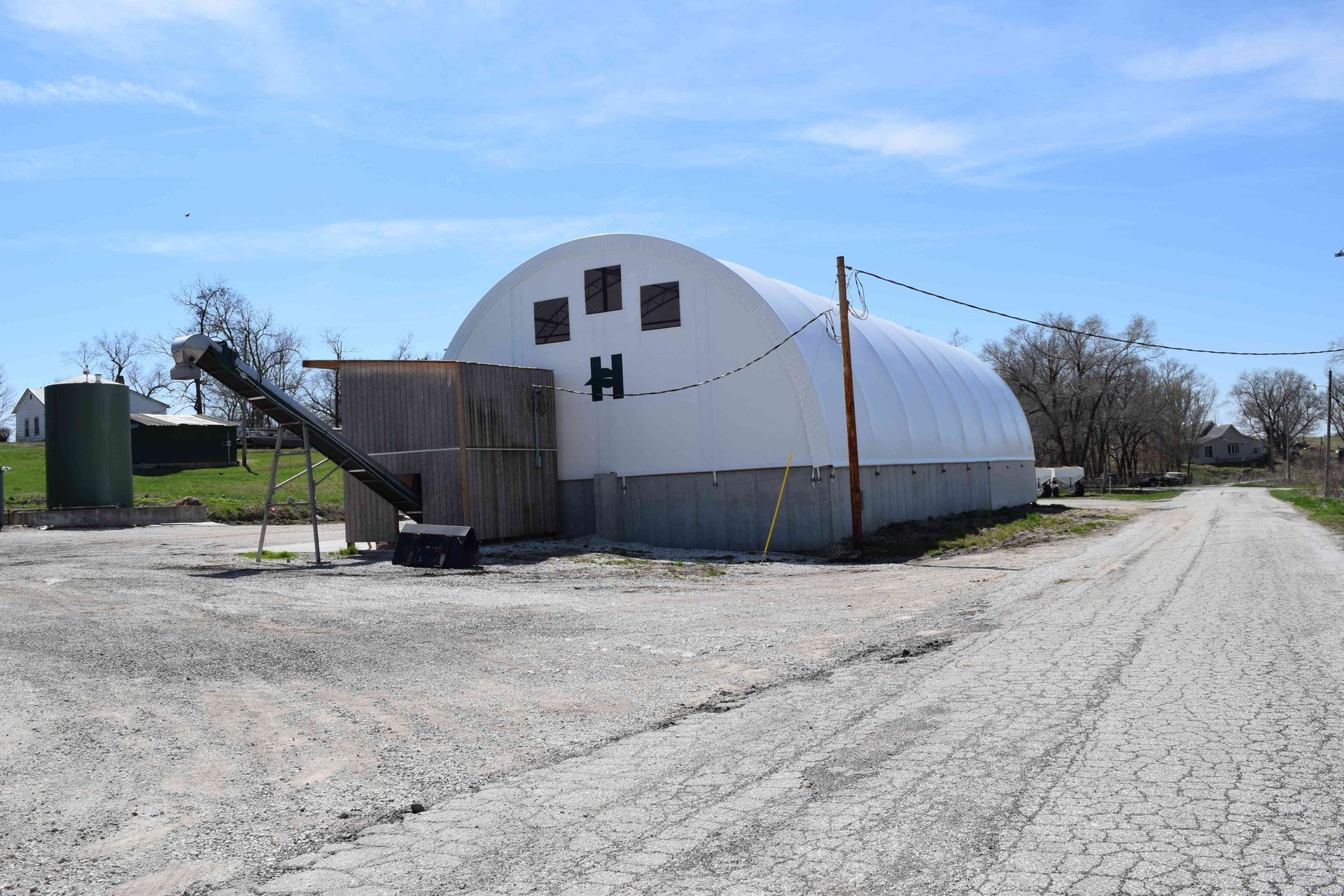 White arched-roof agricultural building with attached wooden structure and gravel road.