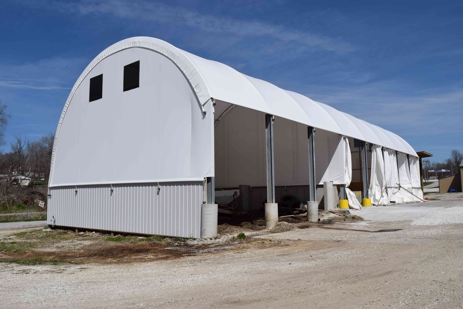 White arched-roof structure with open front, supported by concrete pillars, under blue sky.