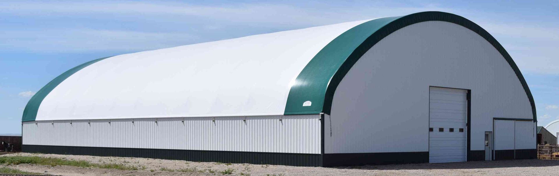 White and green arched warehouse on a field under a blue sky.