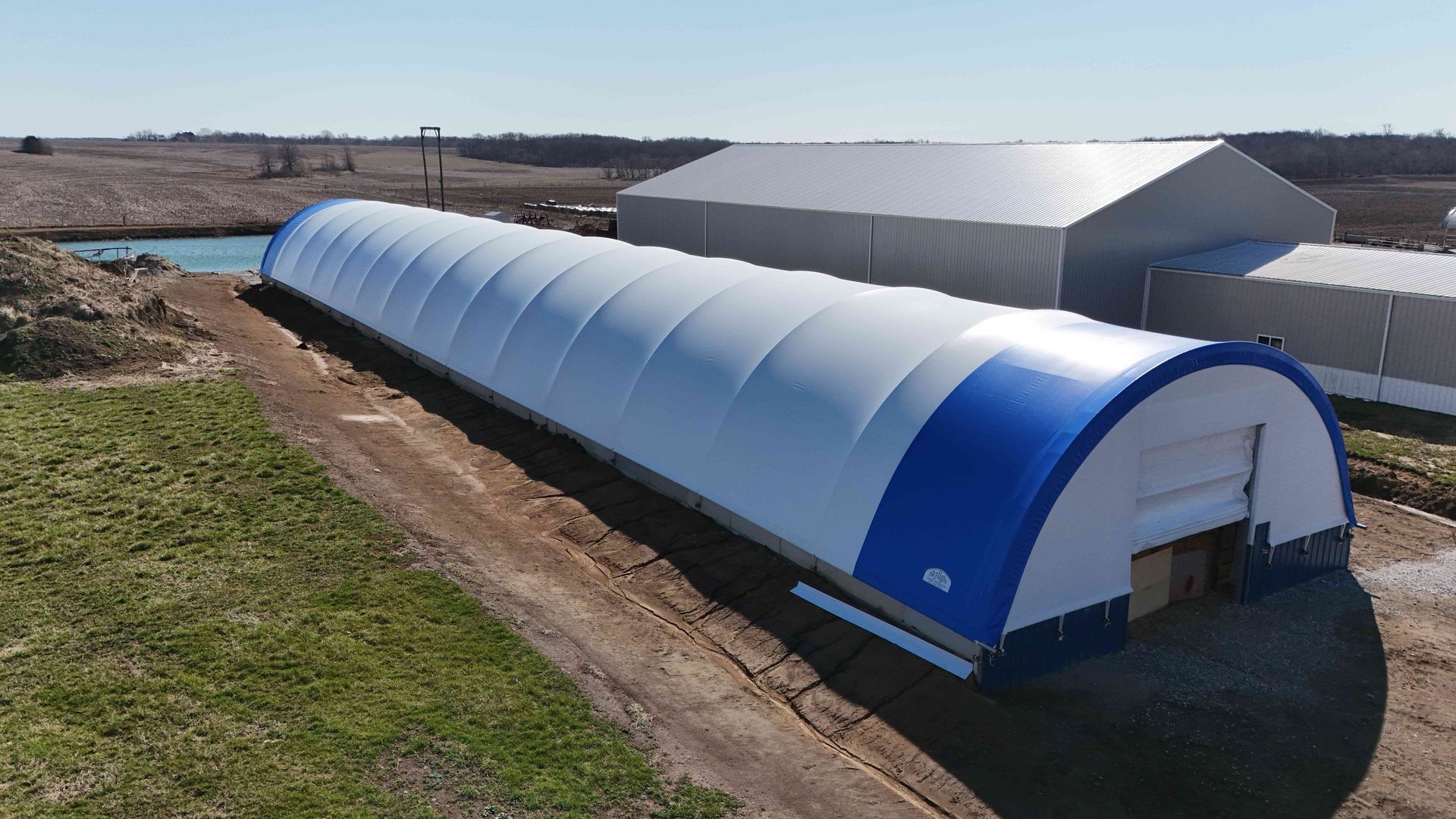 Long, white and blue arched building next to a gray industrial building, situated outdoors.