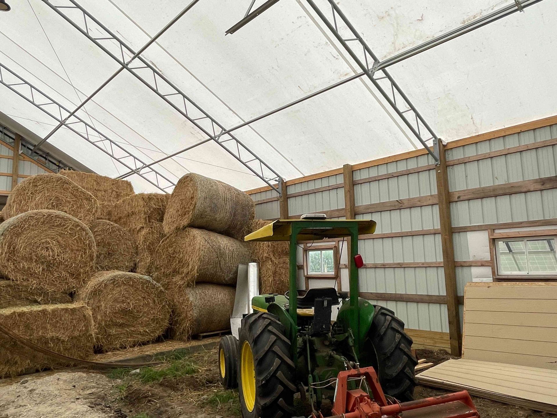 Green tractor in a barn with stacked hay bales.