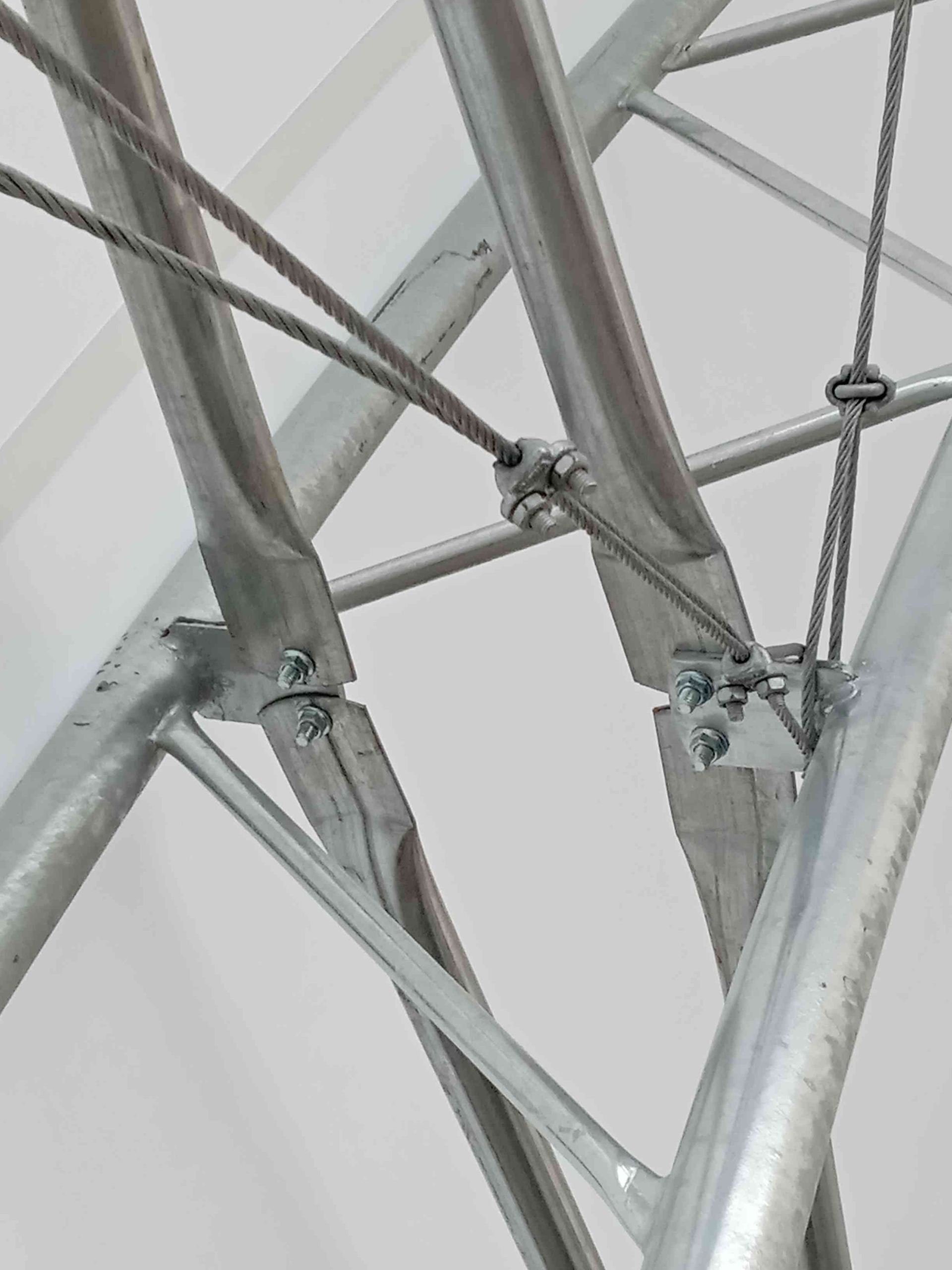 Close-up of a metal structure's joints, with cables and fasteners connecting curved and straight metal beams.