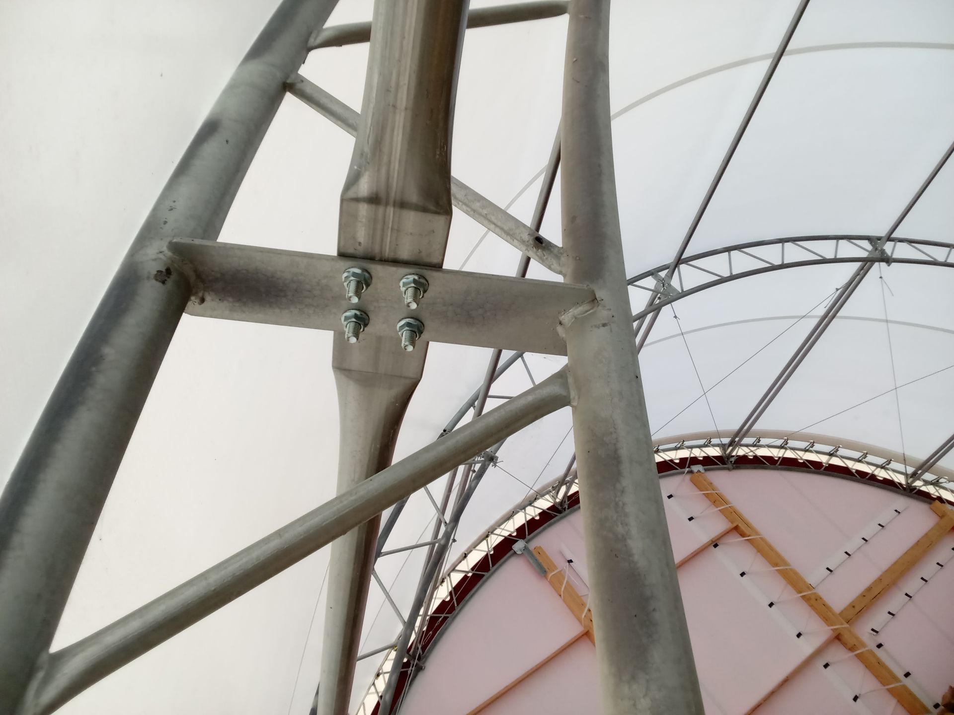 Close-up of a metal structural support system with bolted connections, white fabric roof in background.