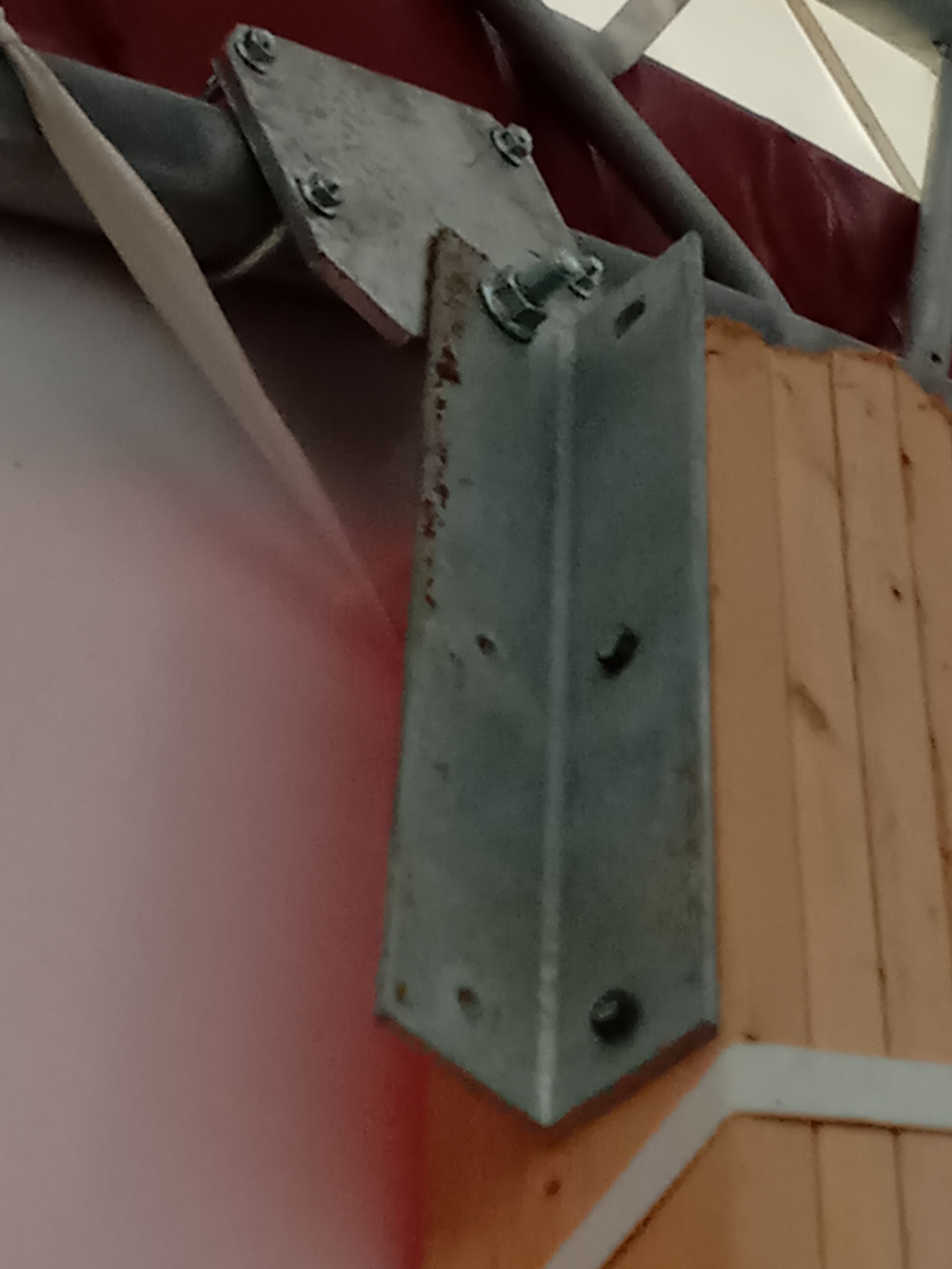 Steel bracket connecting a metal pipe to a wooden structure, against a red wall.