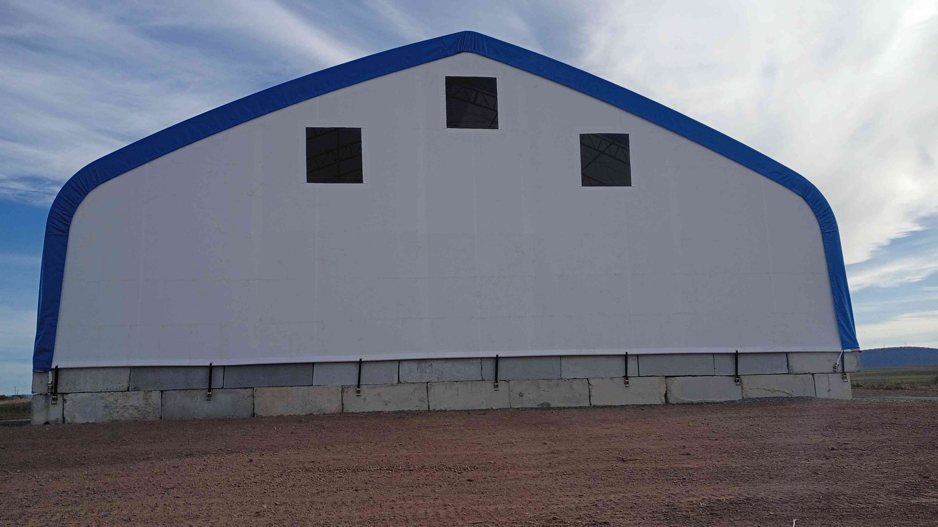 White and blue arched building with three square windows, set on concrete blocks.