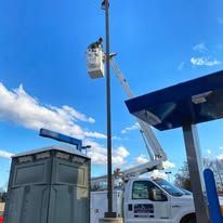 A bucket truck repairing a light pole at a gas station under a blue sky.