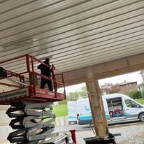 Man on lift working on a metal ceiling in an outdoor setting.