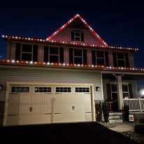 House with Christmas lights along the roof and around the garage doors at night.