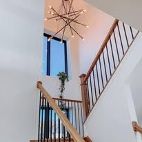 Staircase with modern chandelier, tall window, and wood railing. 