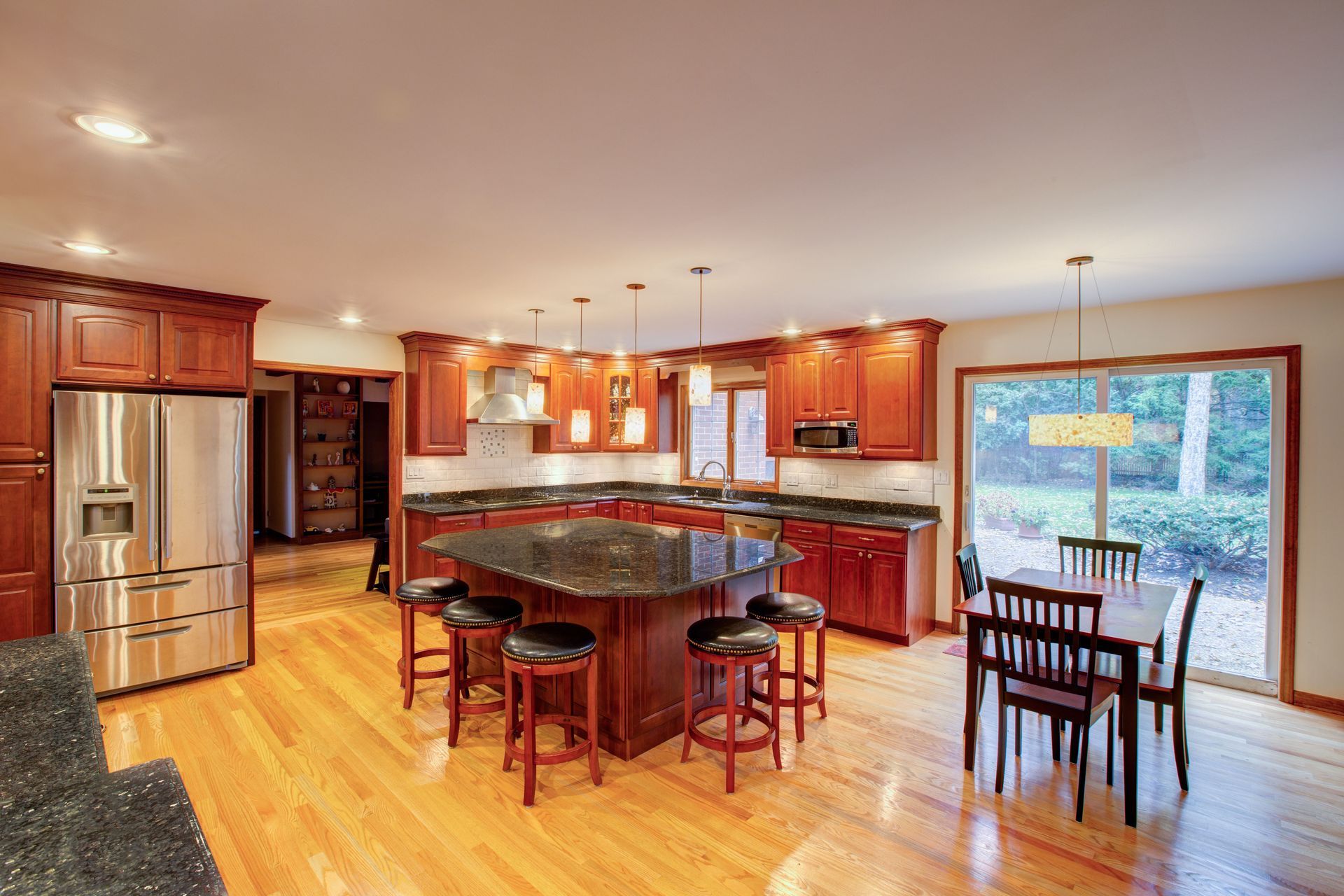 Spacious kitchen with wood cabinets, island with stools, stainless steel fridge, and dining area by window.