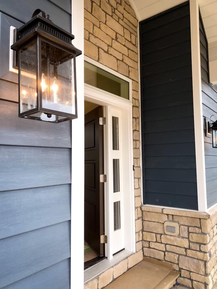 Exterior of a home with blue siding, stone accents, a white door, and a lantern.