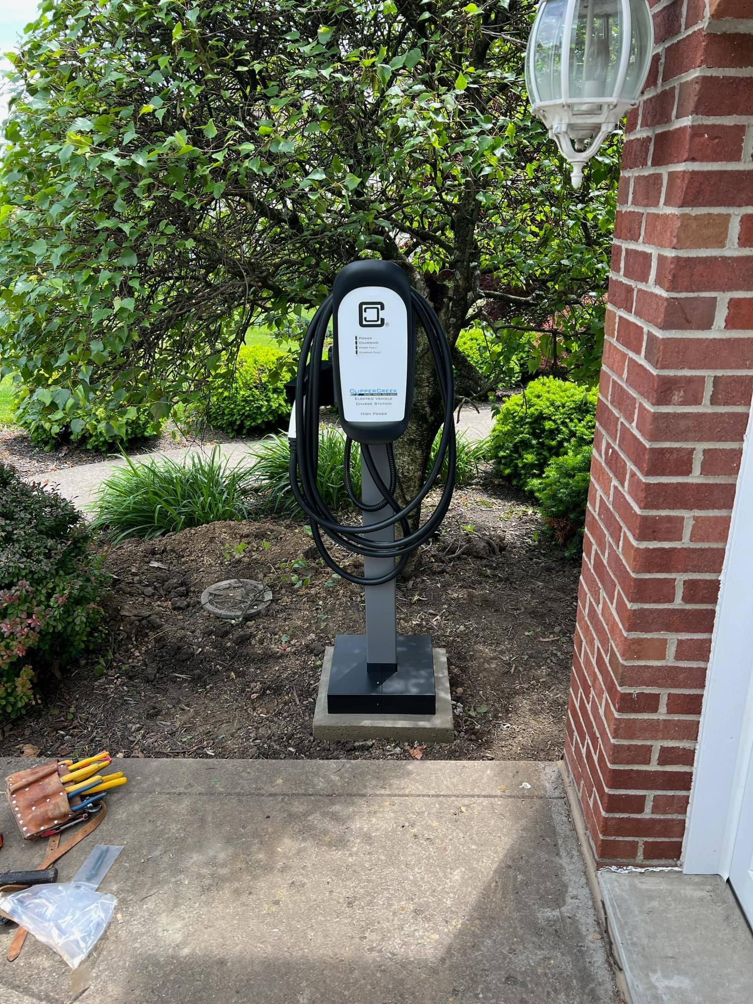 Electric vehicle charger station near a brick building and garden.