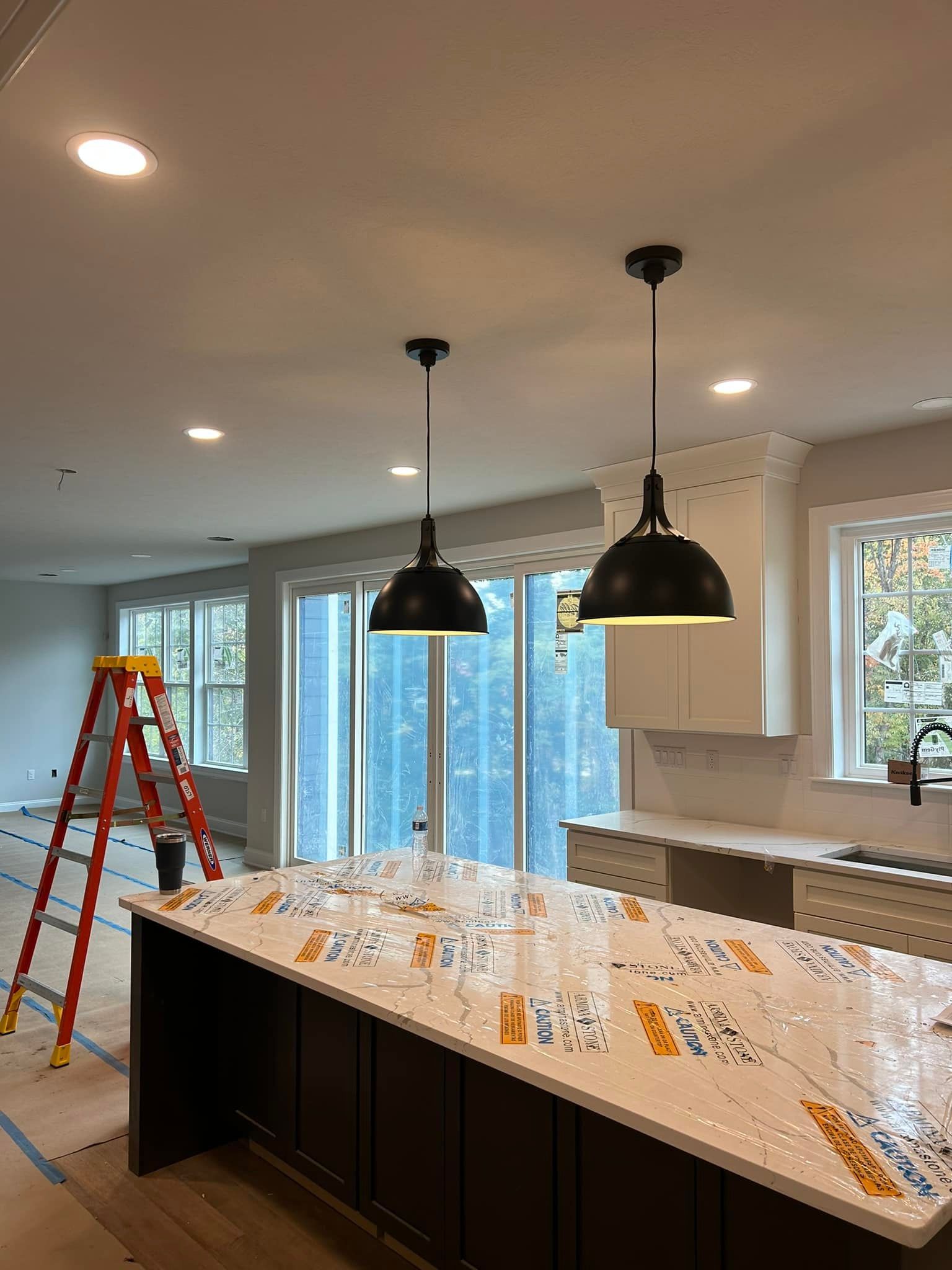 Kitchen with pendant lights, island, and cabinetry. A ladder stands in the adjacent room.