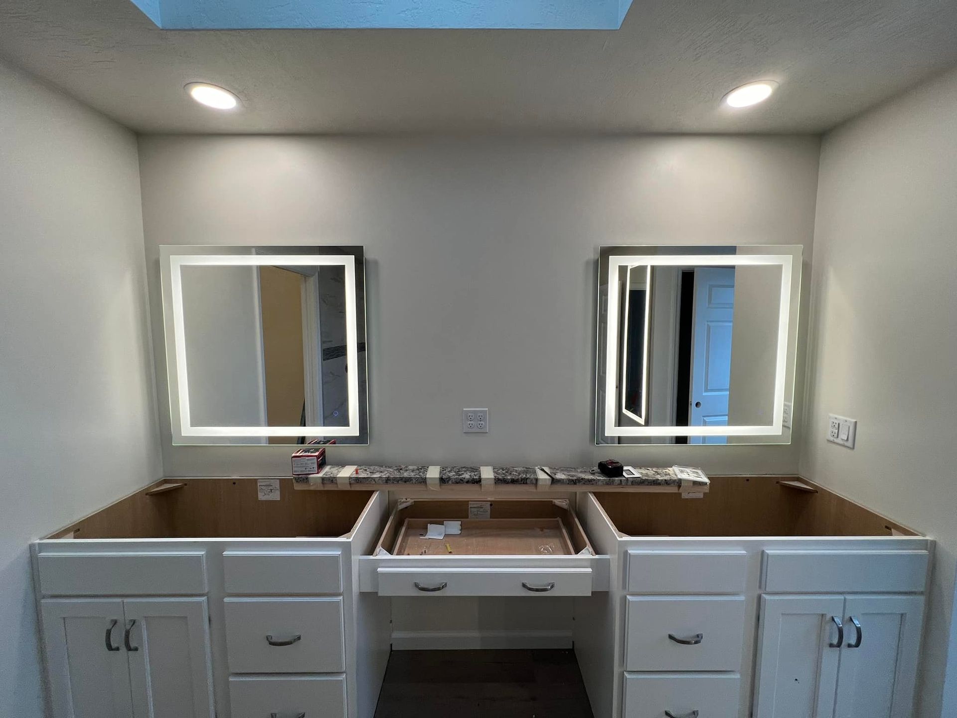 Bathroom vanity with two illuminated mirrors, white cabinets, and center drawer.