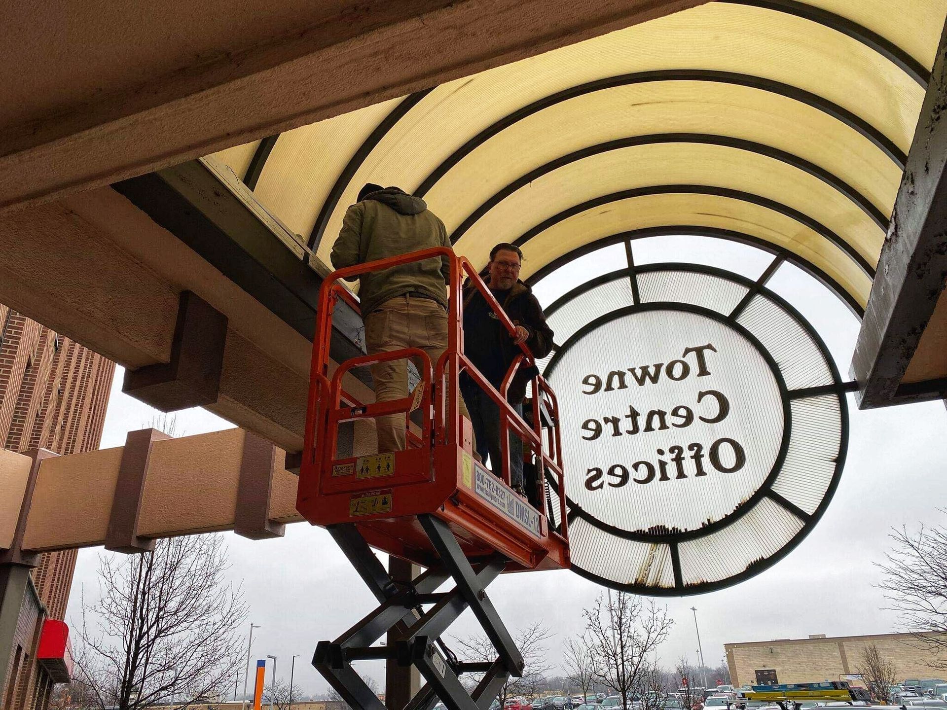 Two people on a lift repair signage that reads 