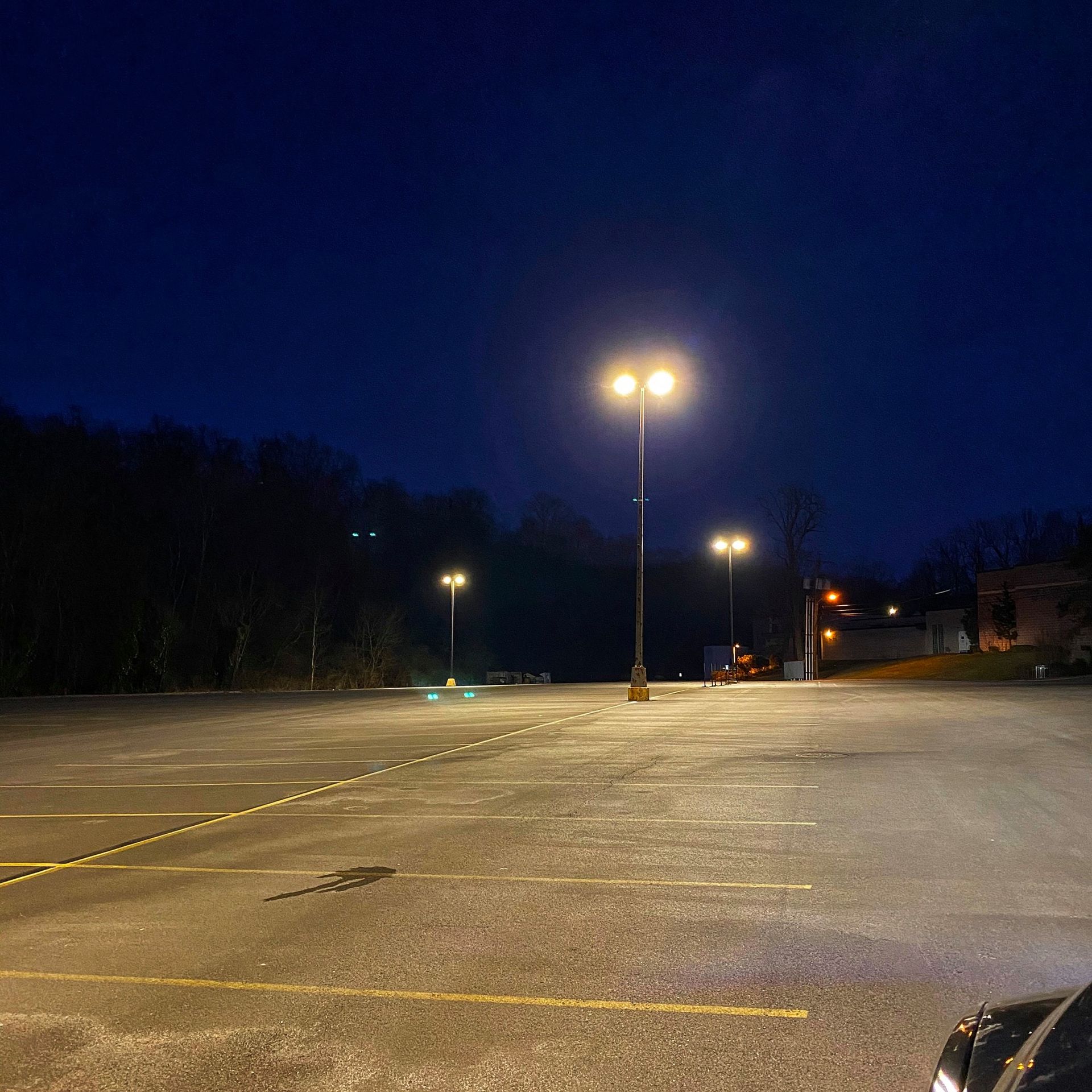 Empty parking lot at night, illuminated by several streetlights against a dark blue sky.