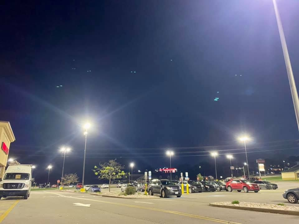 Nighttime parking lot lit by streetlights. Cars parked in rows. 