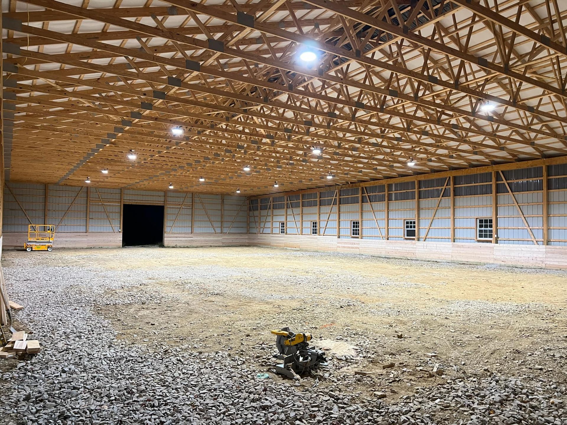 Inside of a large barn under construction, with wood beams and ground covered in gravel.