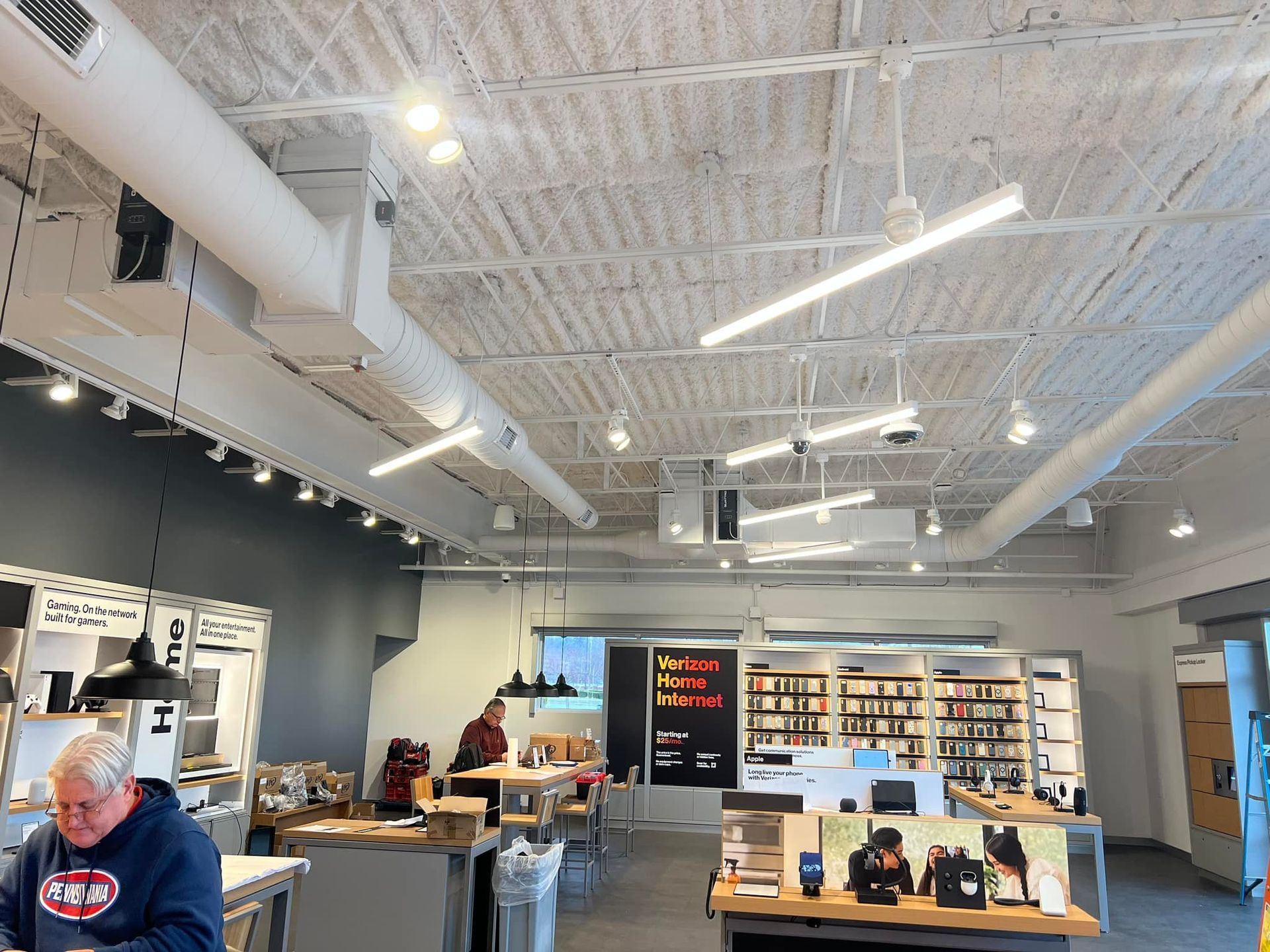 A brightly lit retail store interior with white ceiling, ductwork, and display tables with customers.