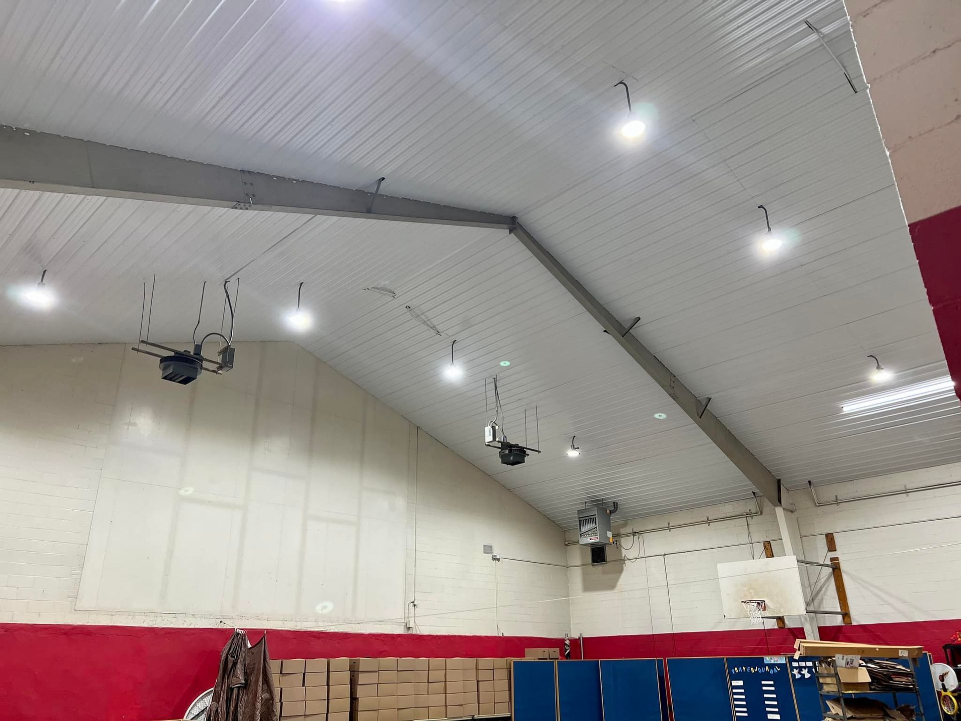 Indoor ceiling with several overhead lights and exposed beams. White corrugated metal ceiling, red and white walls.