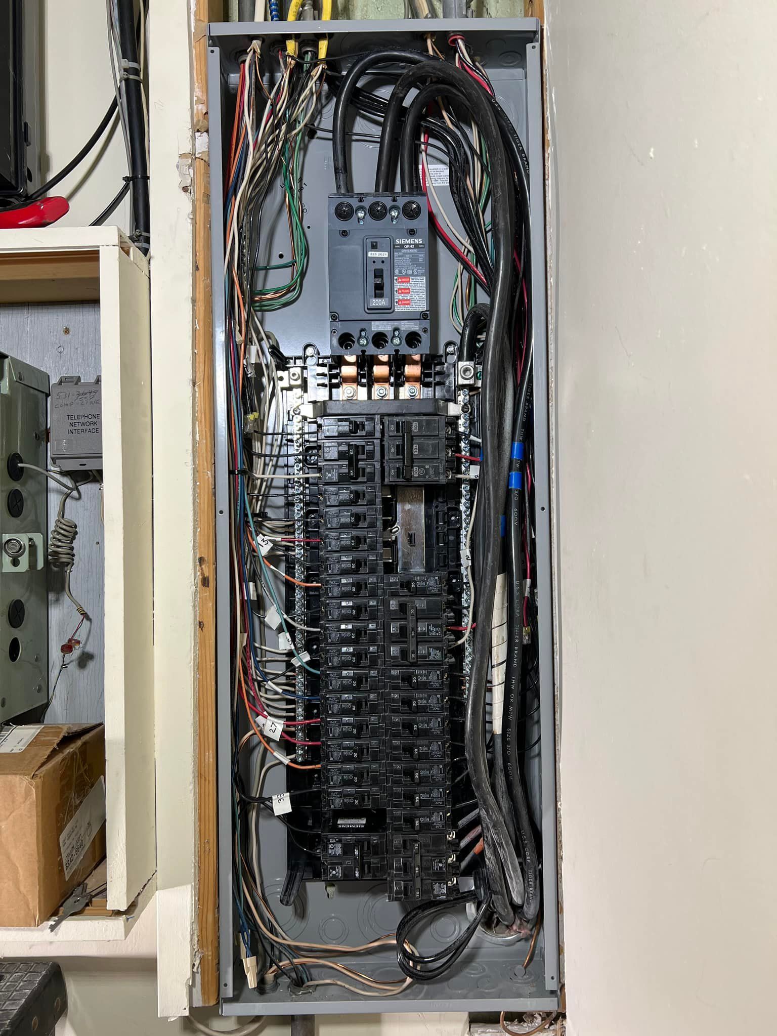 Electrical panel with numerous wires and circuit breakers. Gray panel with black wires visible.