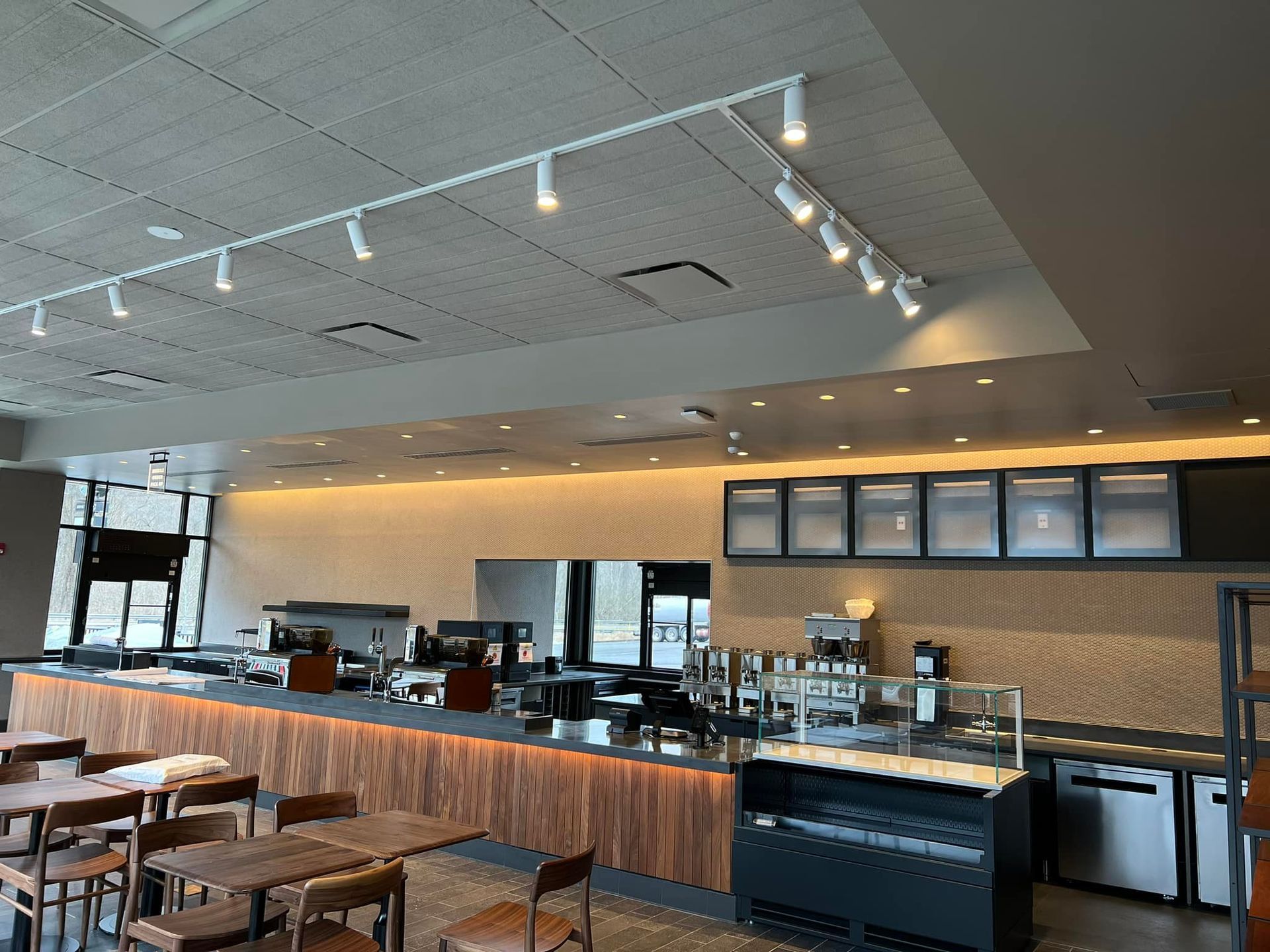 Interior of a Starbucks cafe with a long counter, tables, and track lighting.