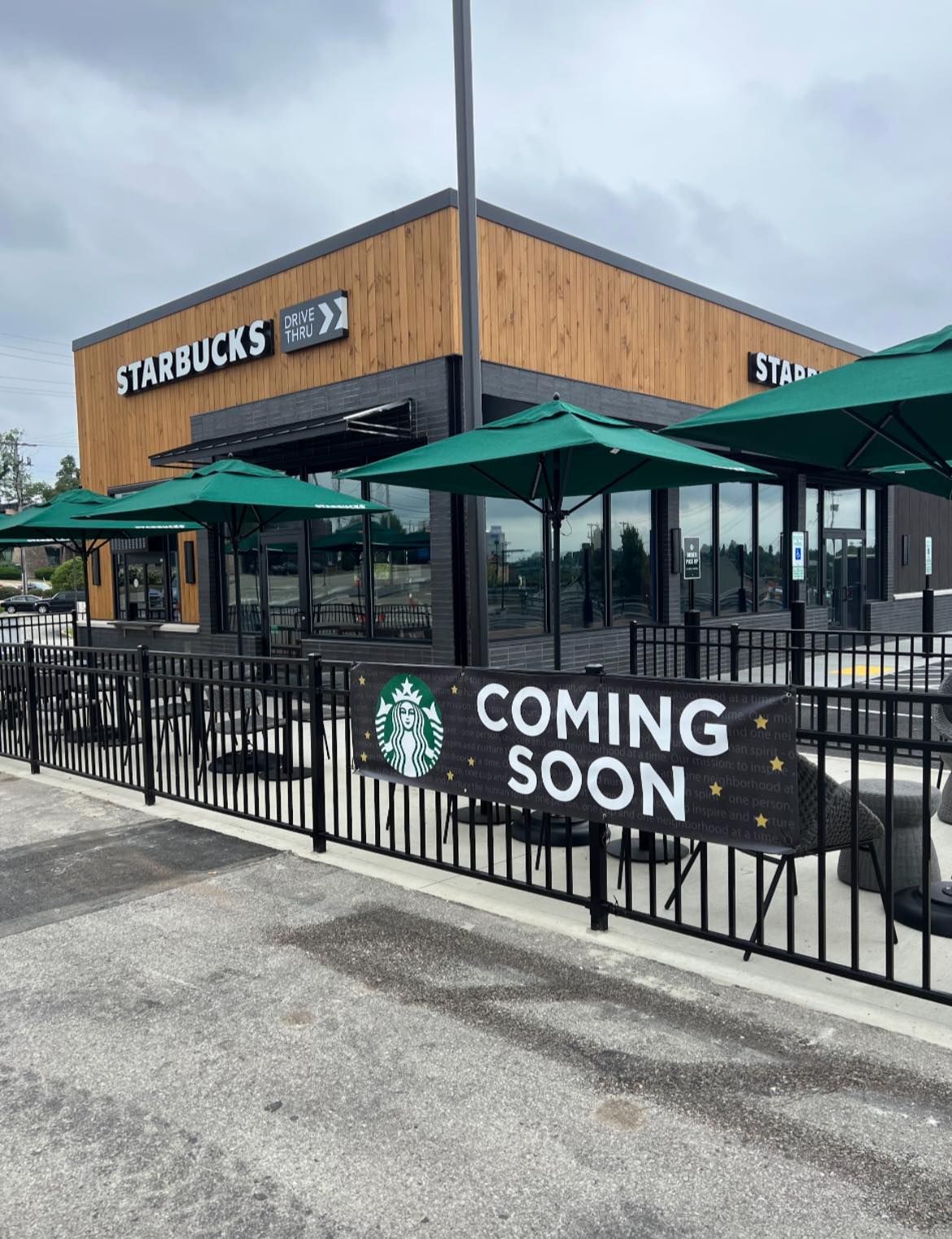A Starbucks store under construction with COMING SOON banner. Exterior view, green umbrellas, black fence.