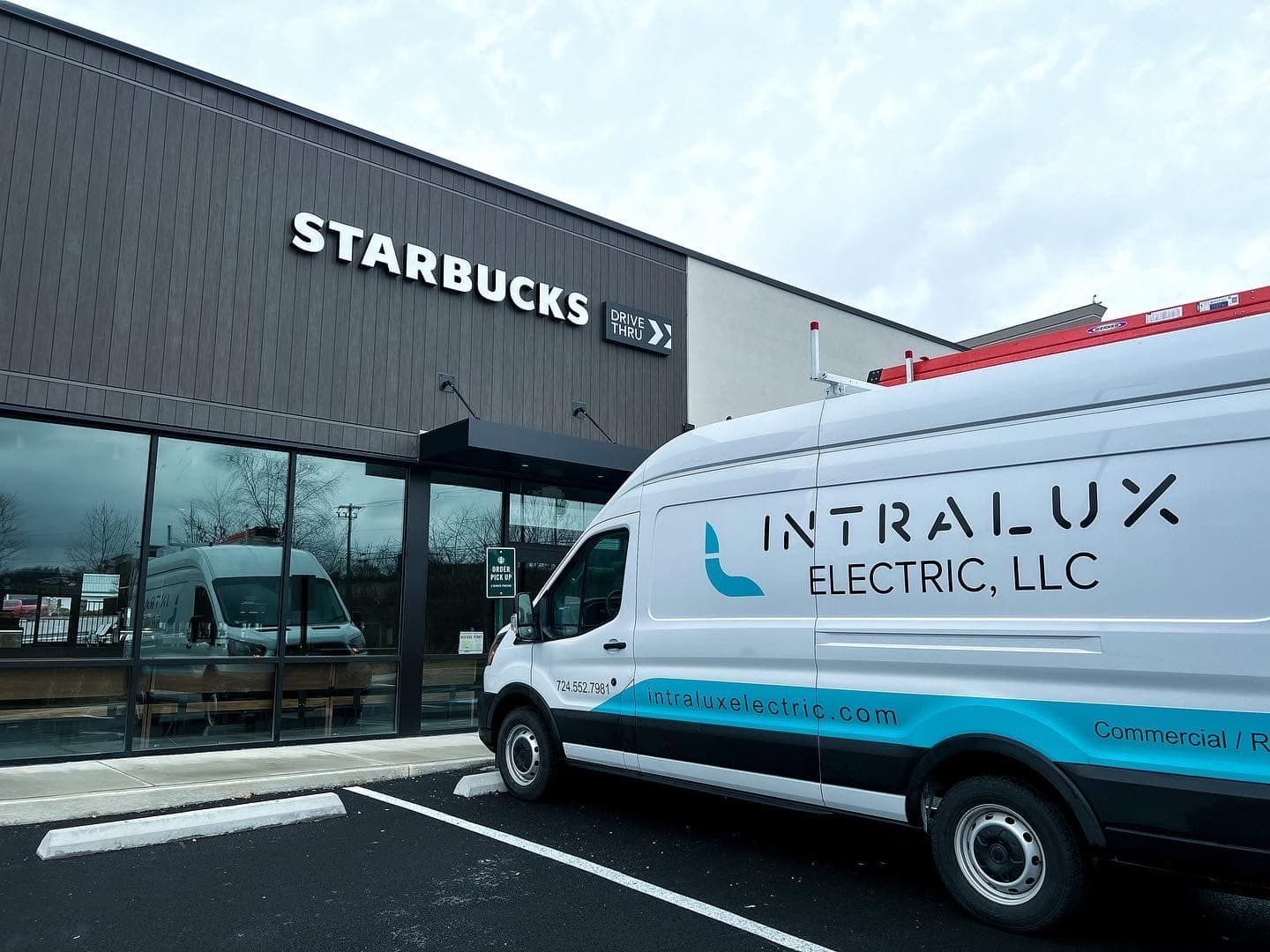 Intralux Electric van parked outside a Starbucks. Dark brown building with large windows.