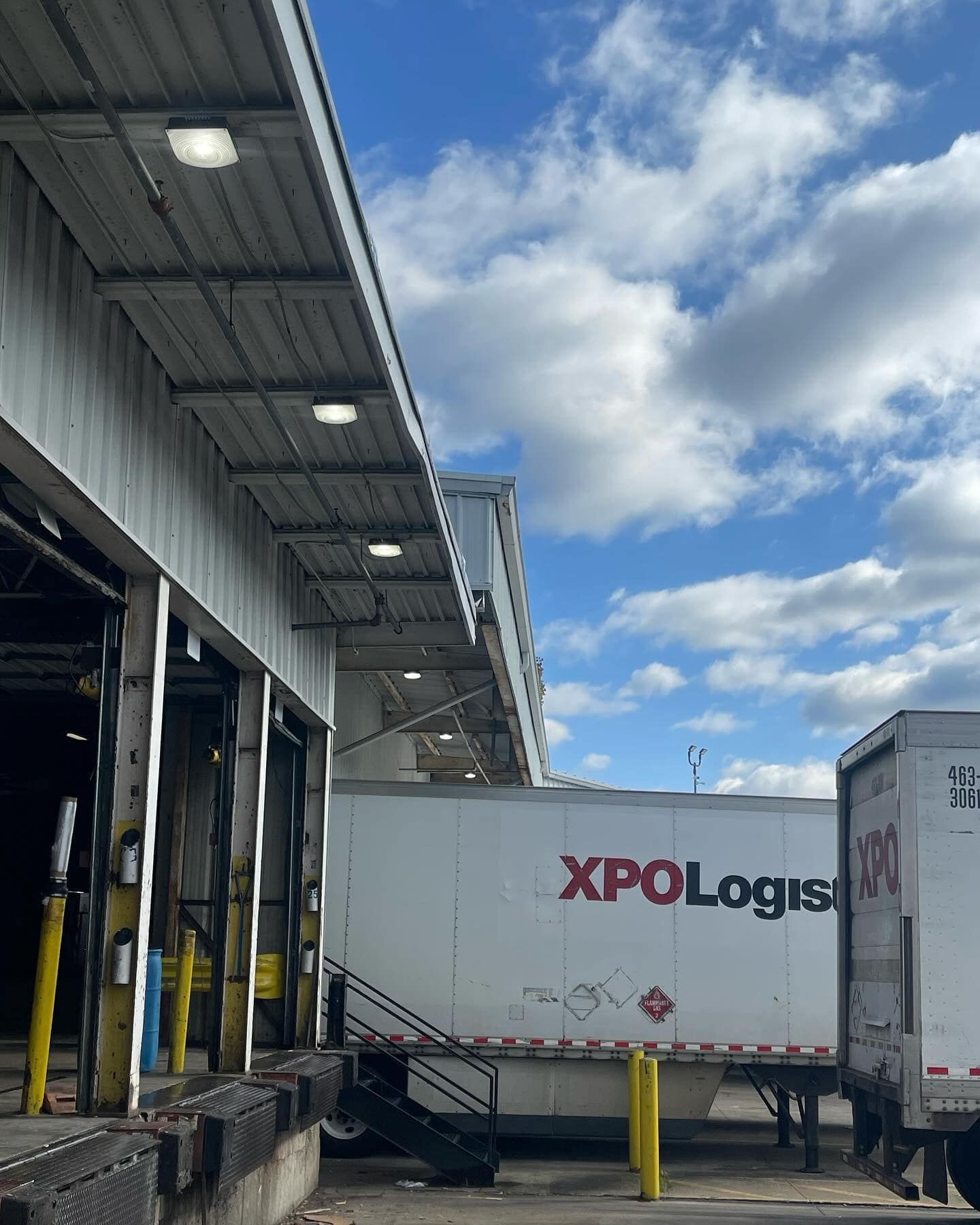 Trucks at loading docks of an XPO Logistics warehouse under a partly cloudy sky.