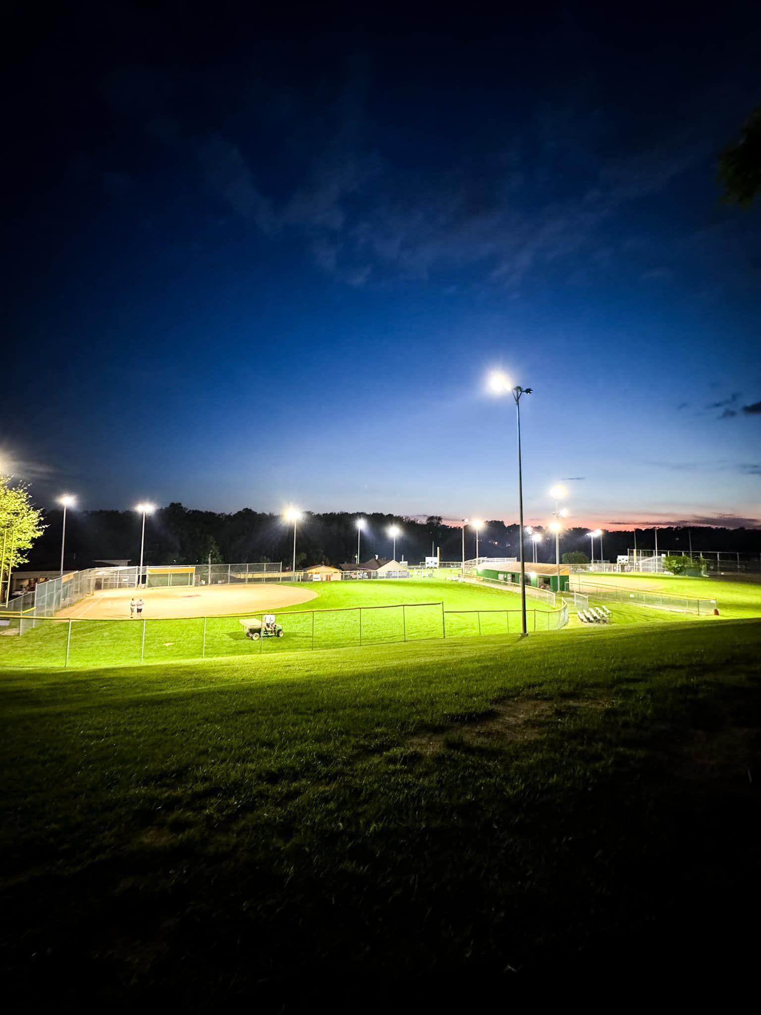 A brightly lit field at dusk, with stadium lights illuminating the green grass and blue sky.