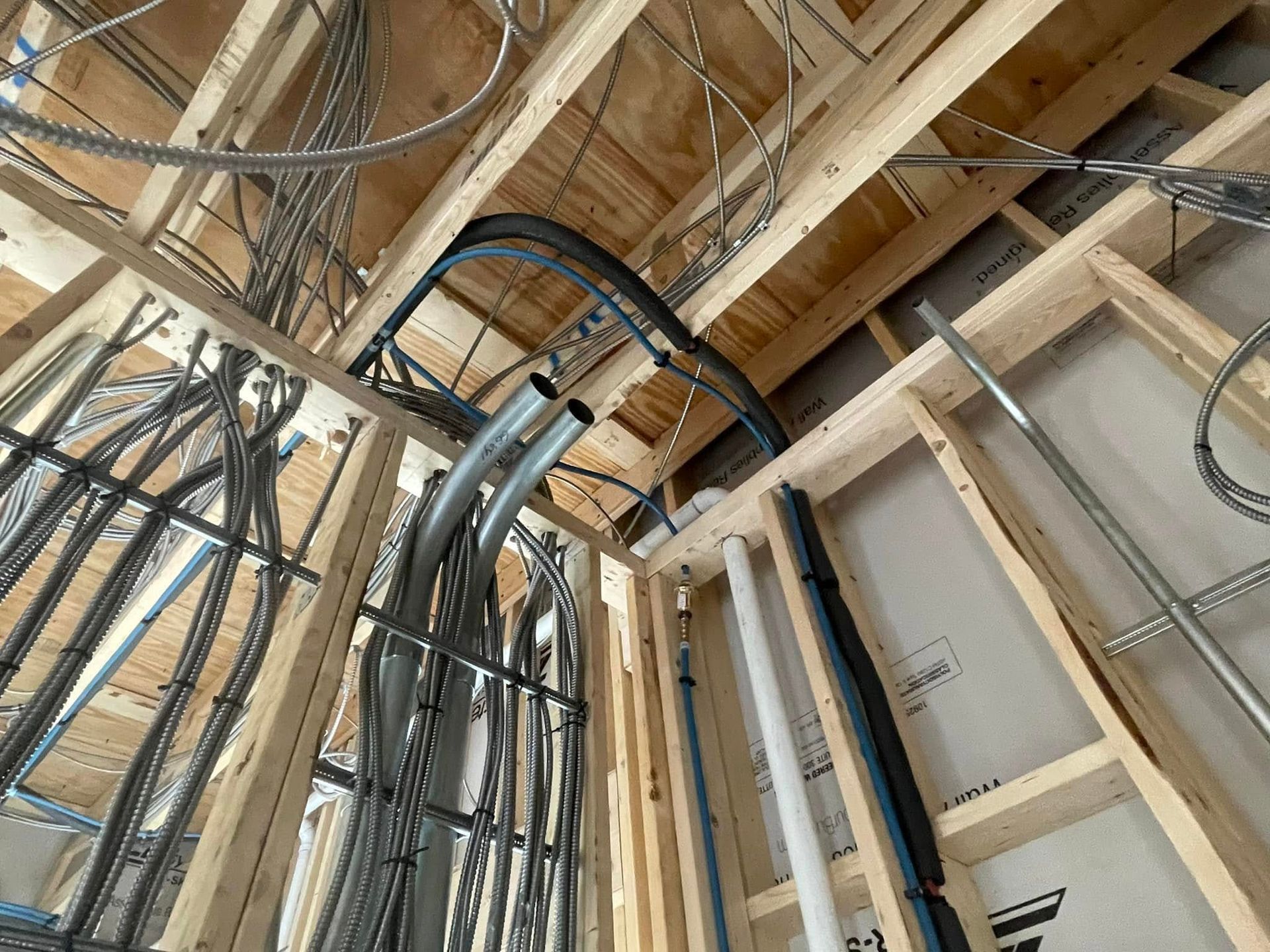 Wooden framework with electrical wiring and pipes installed in a ceiling and walls during construction.