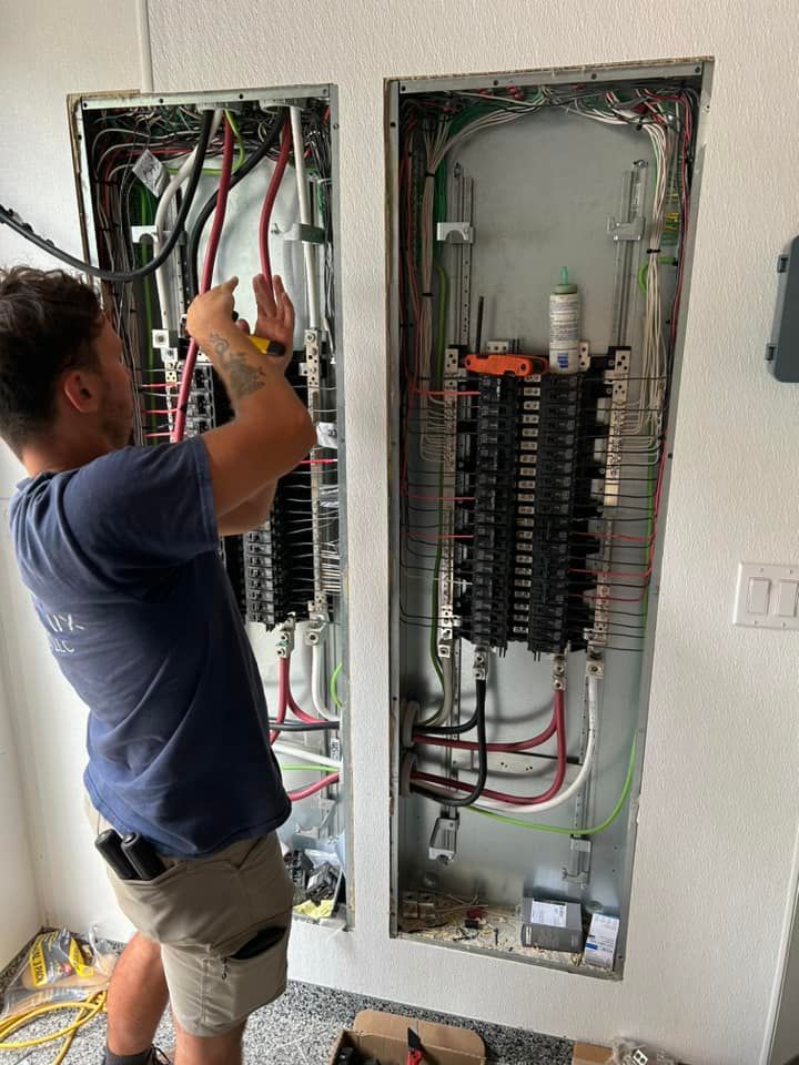 Electrician working on electrical panels in a wall. Wiring and tools are visible.