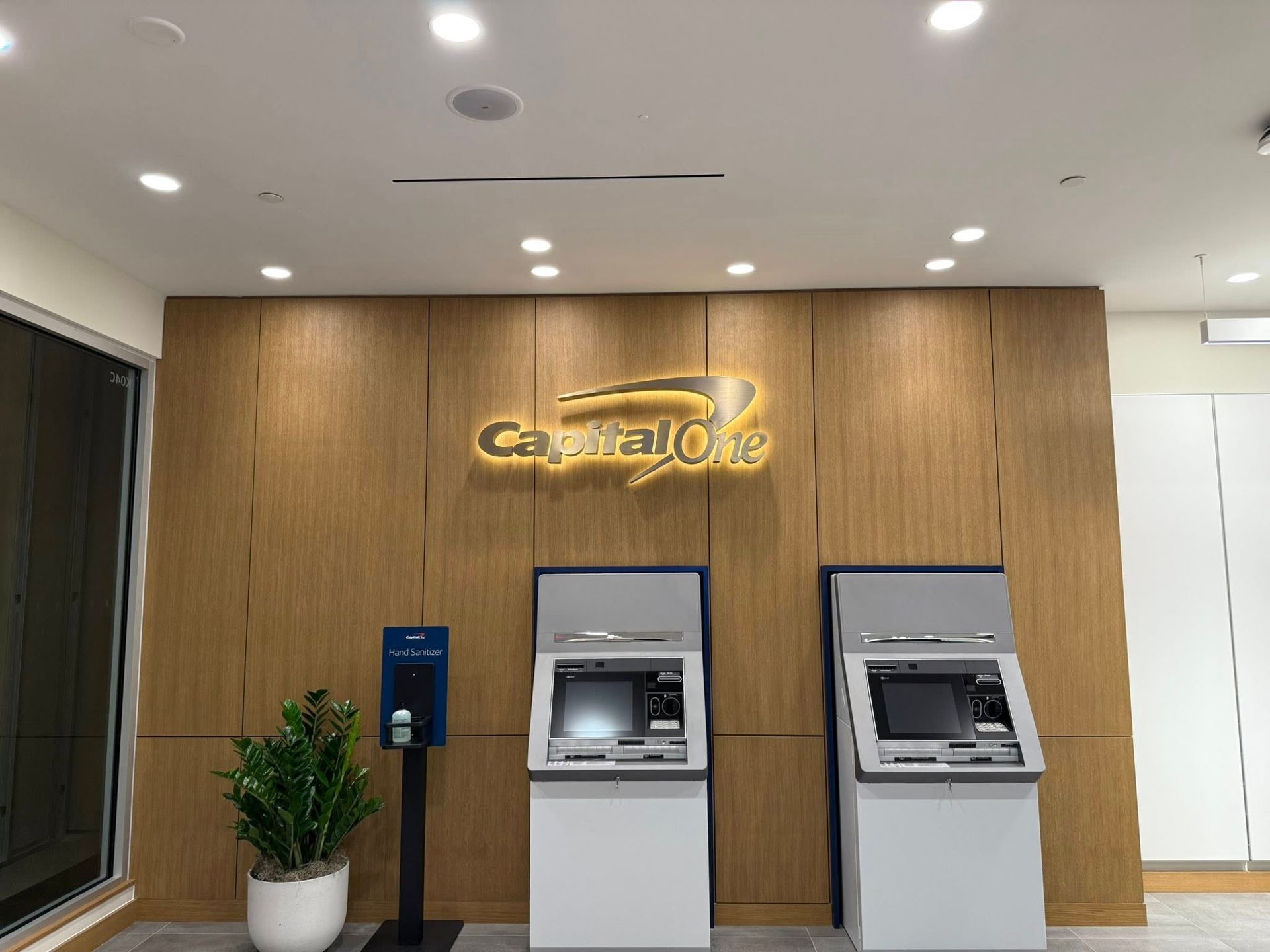 Capital One bank interior with ATMs against a wood-paneled wall, illuminated by overhead lights.