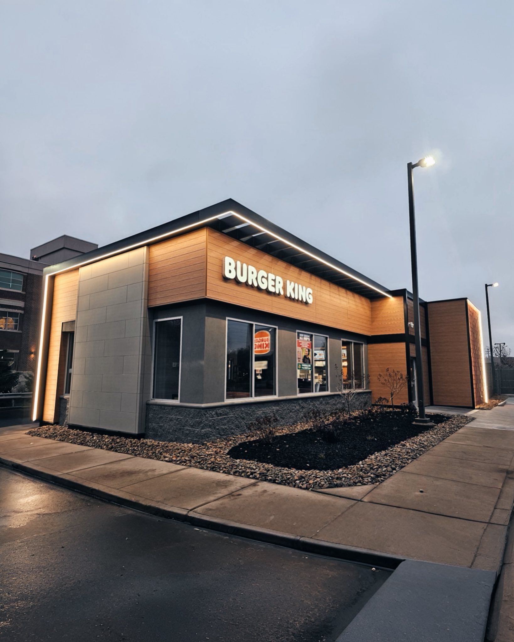 Burger King restaurant exterior, modern design. Tan and dark brick with bright sign and lighting. 