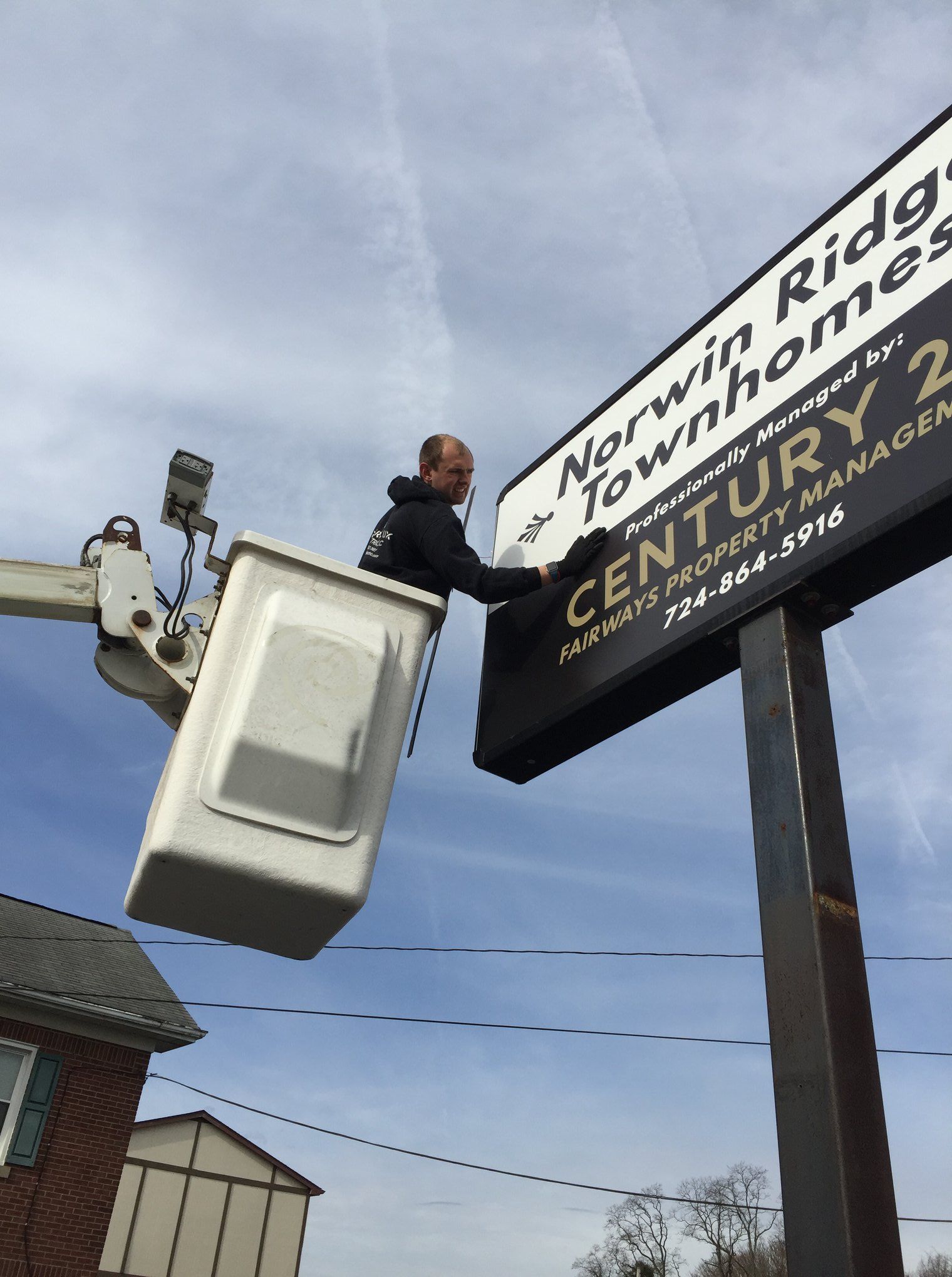 Man in lift bucket adjusts Narwin Ridgeway Townhomes sign, Century 21 contact info visible.