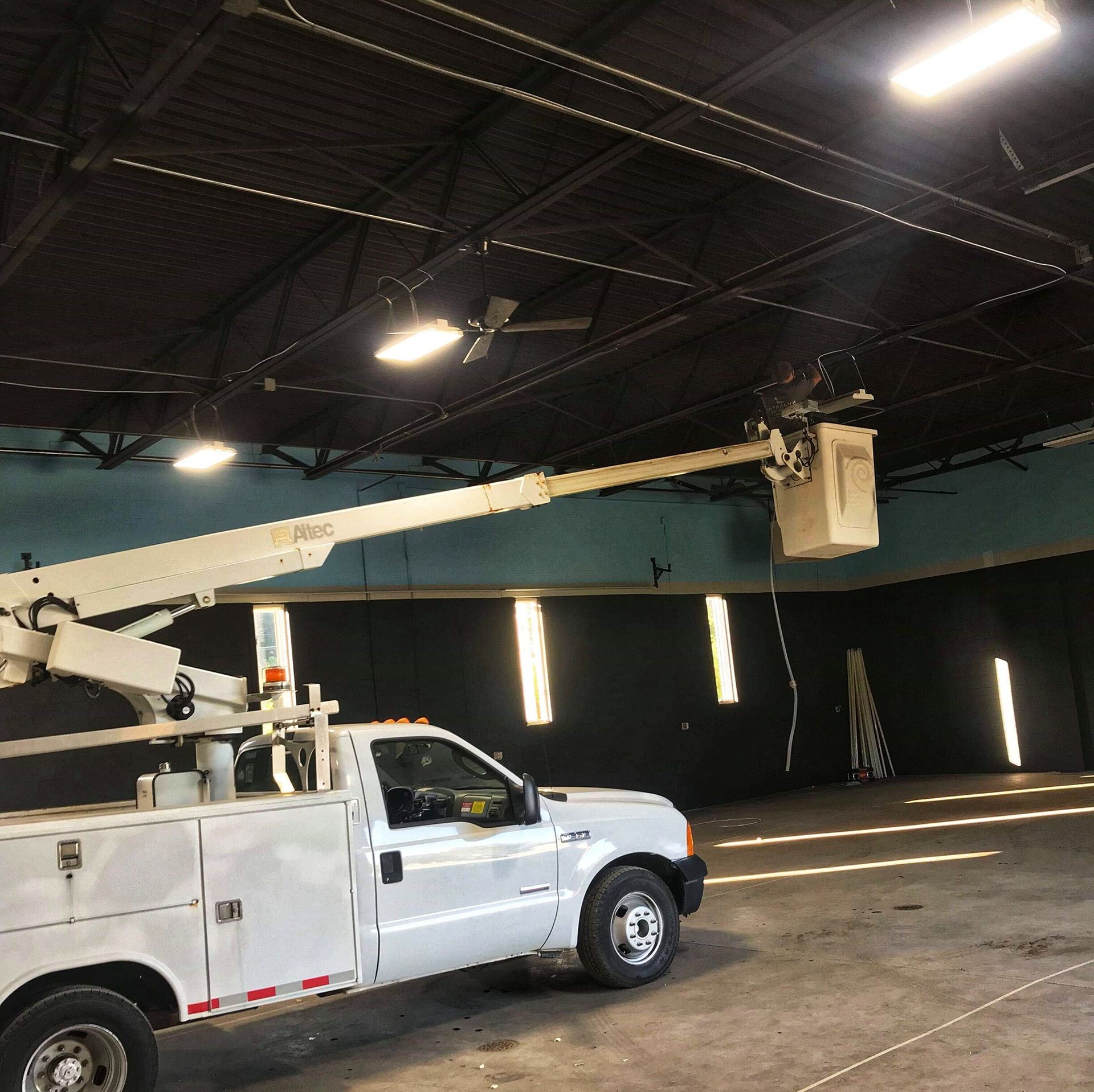 White utility truck with an extended boom, bucket near ceiling, indoors.