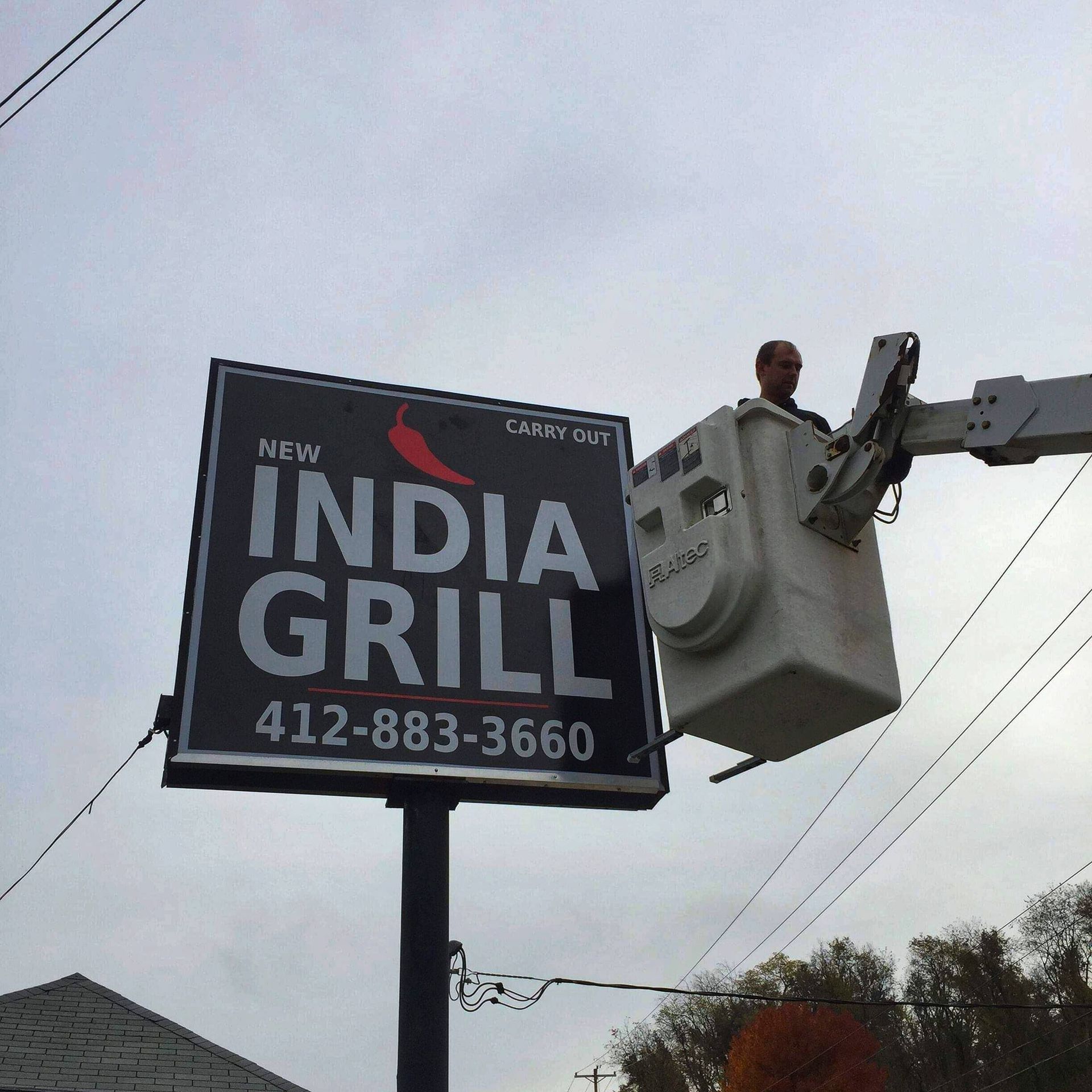 Sign installer in a lift bucket replacing a sign for New India Grill.