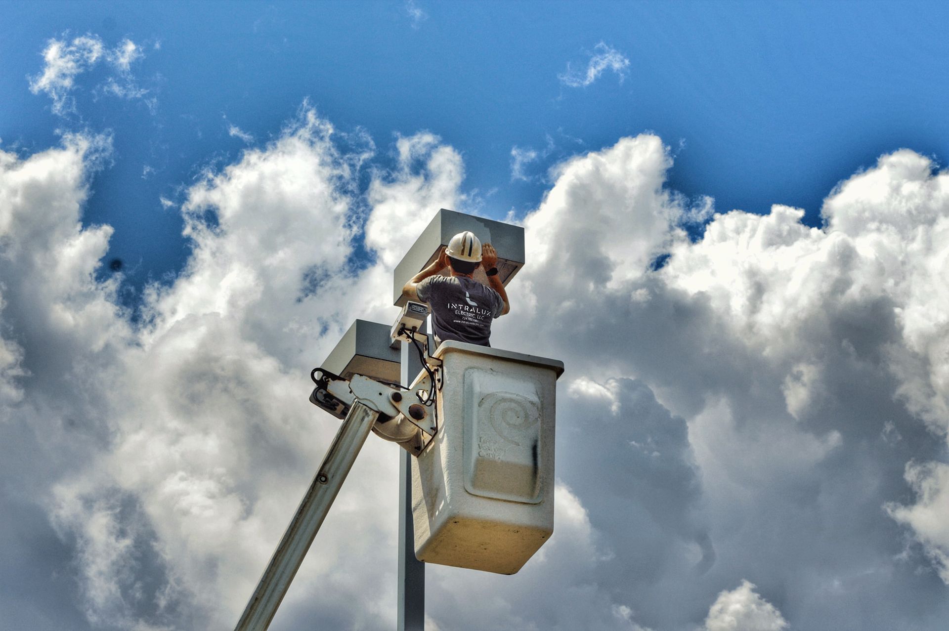 Worker in a bucket lift repairing equipment against a cloudy sky.