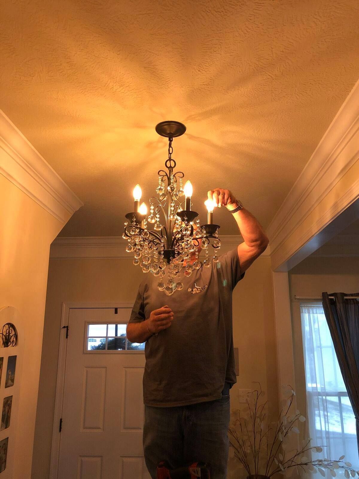 Man standing on a ladder, replacing a lightbulb in a chandelier indoors.