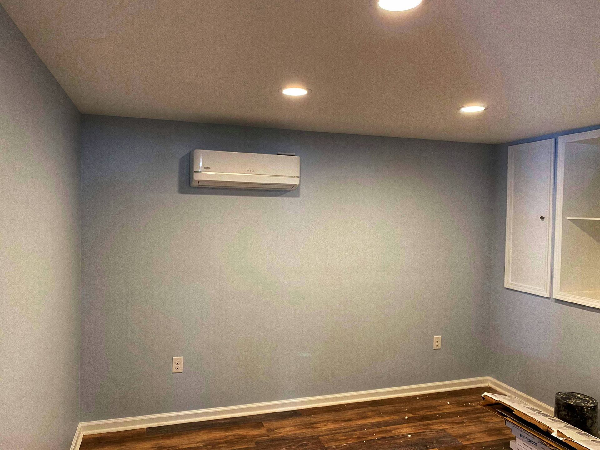 Room with blue-gray walls, wood floor, recessed lights, and a mini-split AC unit on the wall.