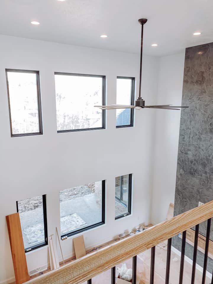 Two-story interior with windows, black frames, white walls, dark ceiling fan, and staircase with railing.