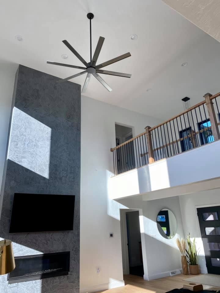 Modern living room with high ceiling, large fan, and a loft.